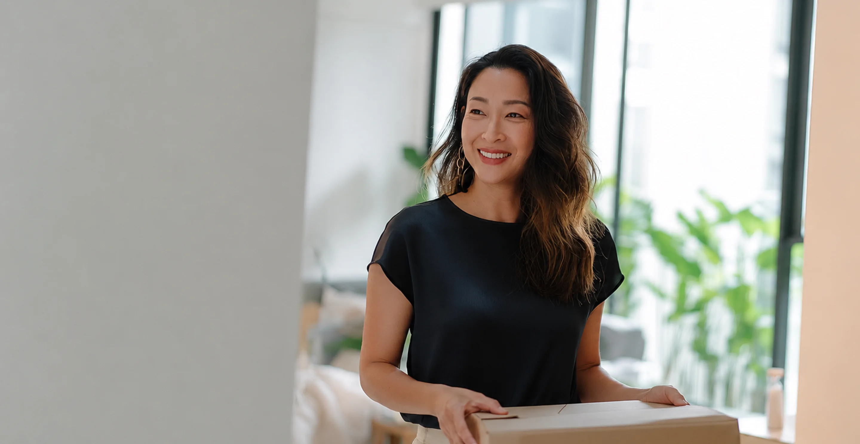 Woman smiling while holding a moving box in a bright apartment